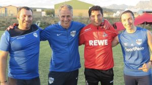 Three coaches of the Young Bafana Soccer Academy and one coach of the 1. FC Cologne standing arm in arm on the pitch of the YB Arena.