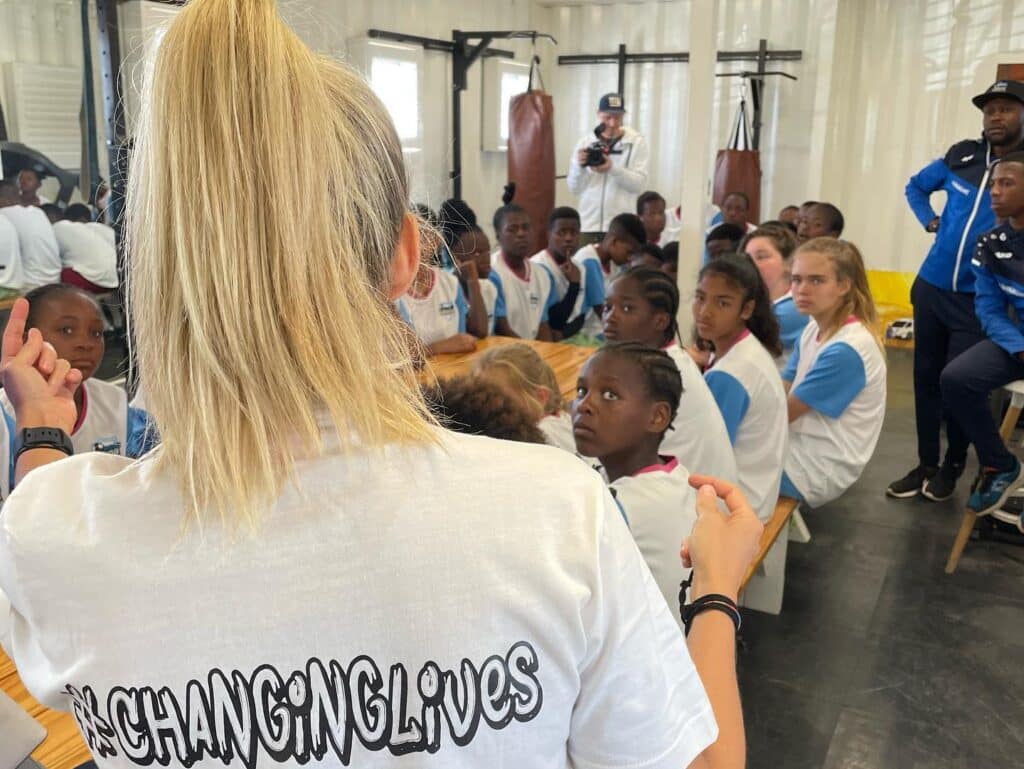 Julia Simic giving a talk in a gym to female soccer players at the Young Bafana Arena during a soccer camp.