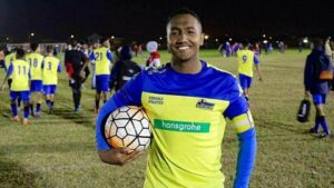 Former Young Bafana player Keino standing on a soccer pitch in South Africa with a football in his hands.